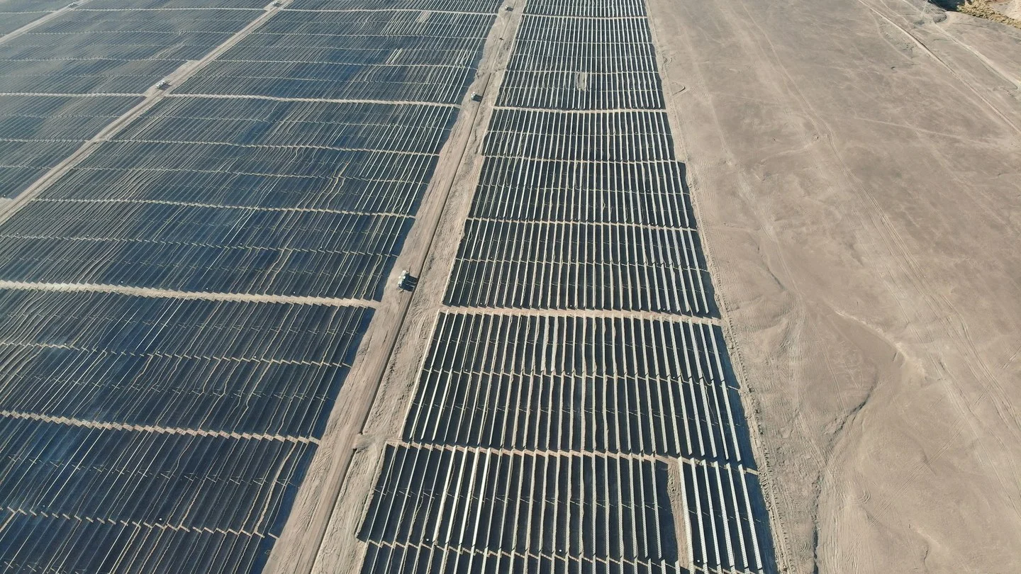 Aerial drone view of a large-scale photovoltaic solar farm in a desert setting, angled rows of panels stretching toward the horizon